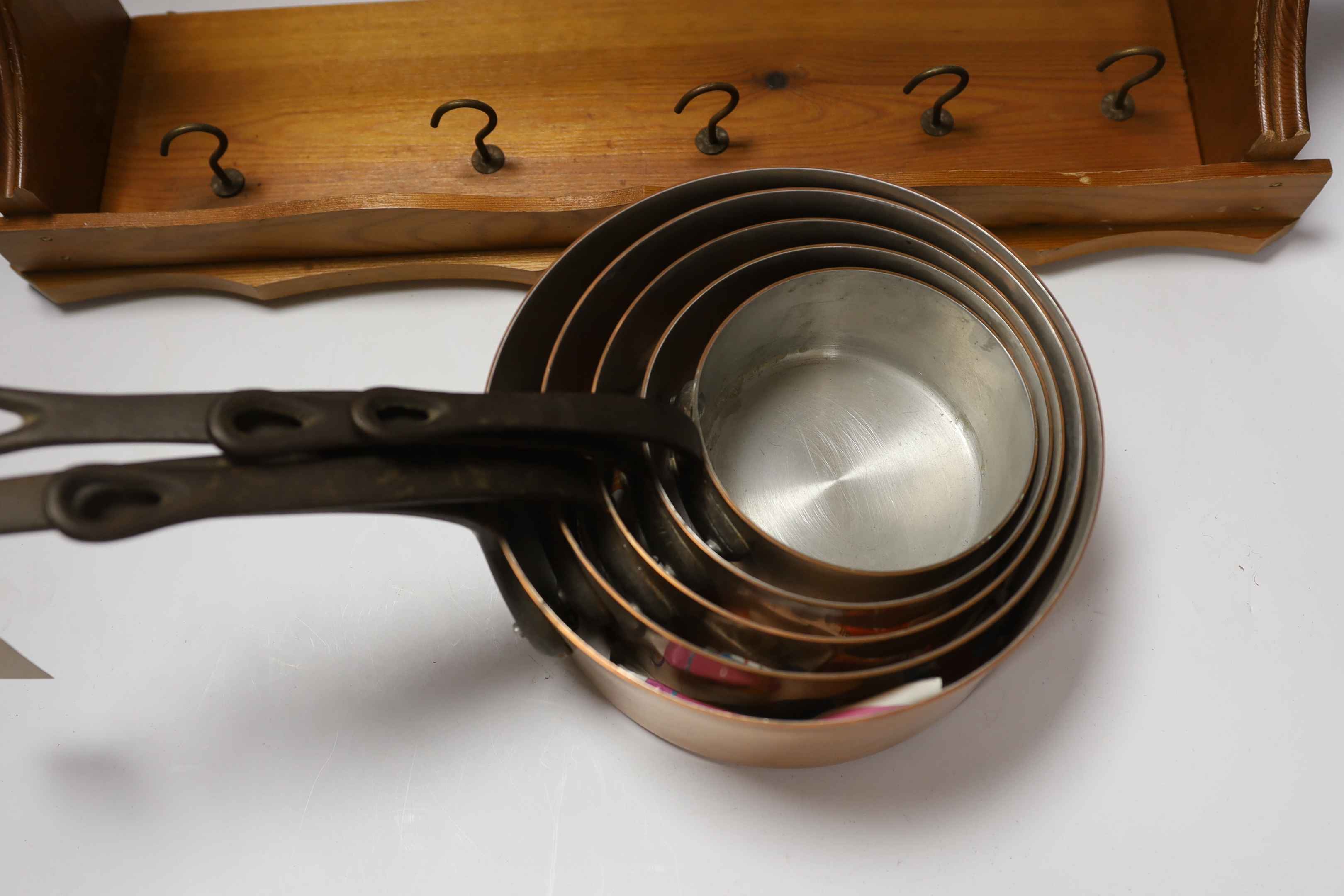 A graduated set of five French copper and cast iron saucepans with pine hanging rack, 57cm wide